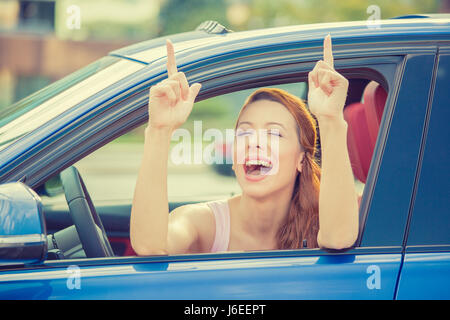 Vue sur la porte latérale conducteur happy smiling woman showing Thumbs up assis à l'intérieur bleu nouvelle voiture à l'extérieur sur l'arrière-plan de stationnement. Belle jeune femme happ Banque D'Images