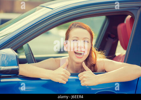 Vue sur la porte latérale conducteur happy smiling woman showing Thumbs up assis à l'intérieur bleu nouvelle voiture à l'extérieur sur l'arrière-plan de stationnement. Belle jeune femme happ Banque D'Images