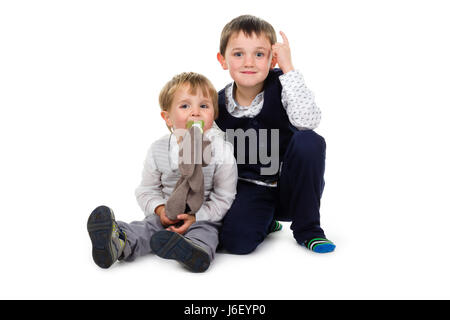 2 Petits frères portant des vêtements de fête, assis ensemble sur le terrain. 1 points un doigt en l'air, l'autre a un animal en peluche brun (rabb Banque D'Images