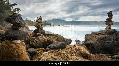 Des pierres empilées, vagues géantes, et montagnes luxuriantes sur un jour nuageux sur la côte nord d'Oahu, Hawaii. Banque D'Images