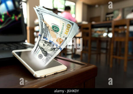 Téléphone mobile avec des dollars qui sortent concept sur table en bois dans la région de coffee shop fond , copie espace . Stock Trading où chaque concept. Banque D'Images