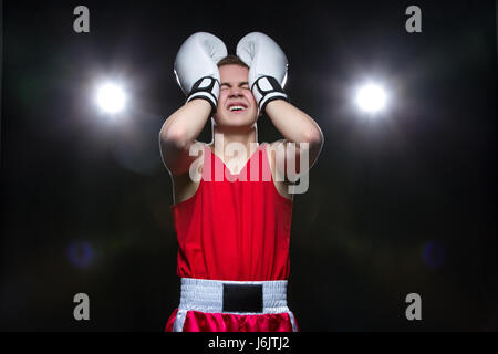 Déçu teenage boxer dans forme rouge et gants blancs, rétro-éclairage. Studio shot sur fond noir. Copier l'espace. Banque D'Images