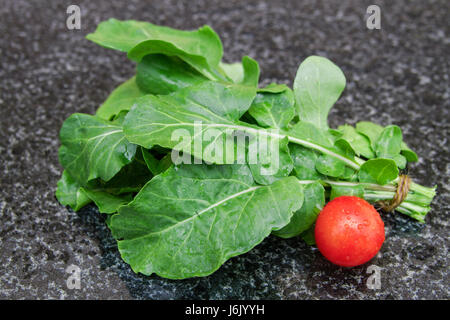 Paquet de roquette (rukola) avec tomates, roquette fraîche (fusée) feuilles de salade sur une table en granit. Banque D'Images