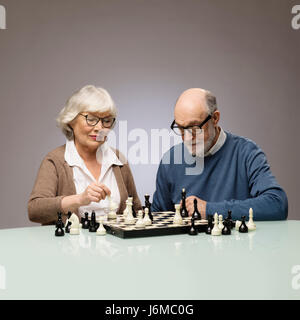 Vieux couple jouant aux échecs, studio shot sur fond gris Banque D'Images