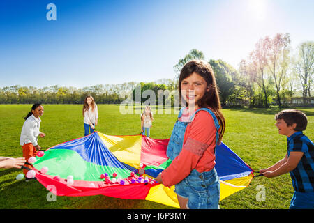 Portrait de jeune fille debout dans un cercle avec ses amis et maintenant plein de parachute arc-en-ciel boules colorées Banque D'Images