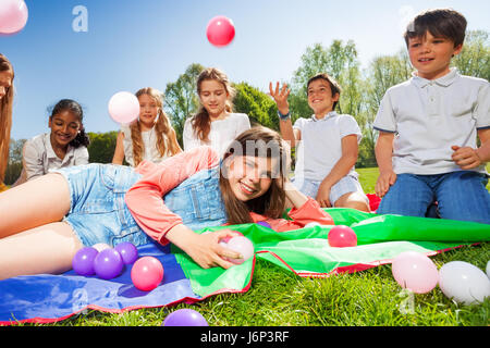 Portrait of happy girl laying on mat entouré par ses amis, dresser des boules colorées en été park Banque D'Images