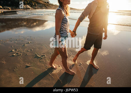 Tourné en plein air d'aimer les jeunes couple en train de marcher sur le bord de la mer se tenant la main. Jeune homme et femme marche sur la plage ensemble.