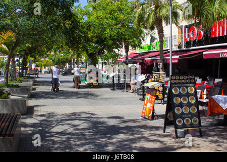 Les touristes la marche et coin sur une avenue bordée d'arbres avec des boutiques et des cafés à Playa de Las Americas, sur l'île de Ténériffe Banque D'Images