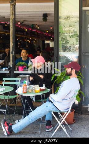 Jeune beau couple de casquettes de baseball de manger à une table à l'extérieur d'un restaurant vietnamien à SoHo, New York City, regardant un travail de construction. Banque D'Images