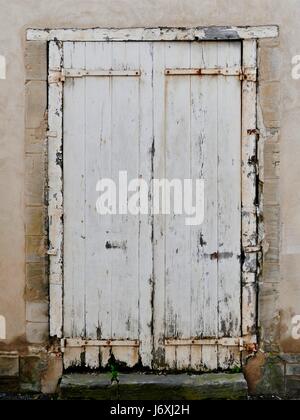 Vieux, blanc, bois, double porte avec bords pourris. Métal rouillé. Off white, bâtiment en pierre. Bayeux, Calvados, France. Banque D'Images