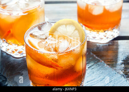 Thé glacé au citron et tranches de pêches et des cubes de glace sur l'ardoise et rustique en bois historique close up. Boisson d'été rafraîchissante faite maison. Banque D'Images
