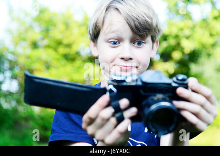 Sad boy à ouvrir à l'arrière de l'appareil photo et film à l'intérieur ruiné éclairé. Petit enfant garçon blond avec un ancien appareil photo shooting en extérieur. Kid tak Banque D'Images