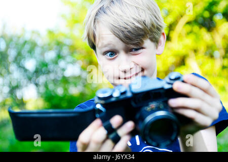 Sad boy à ouvrir à l'arrière de l'appareil photo et film à l'intérieur ruiné éclairé. Petit enfant garçon blond avec un ancien appareil photo shooting en extérieur. Kid tak Banque D'Images