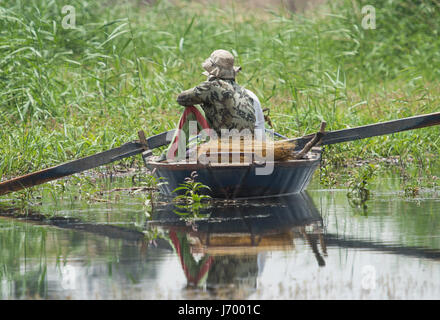 Pêcheur bédouin traditionnel égyptien en bateau à rames sur la rivière du Nil la pêche par l'herbe des berges de roseaux Banque D'Images