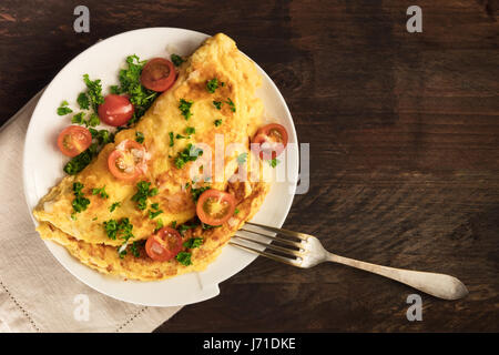 Une photo d'une omelette aux tomates cerises, le persil et le fromage râpé, tourné à partir de ci-dessus sur une texture rustique en bois avec une place pour le texte Banque D'Images