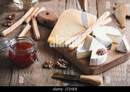 Assiette de fromage servi avec du vin blanc, de confiture et de noix sur planche de bois sur la table rustique Banque D'Images