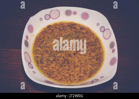 Soupe aux nouilles orzo dans bol blanc sur la table en bois Banque D'Images