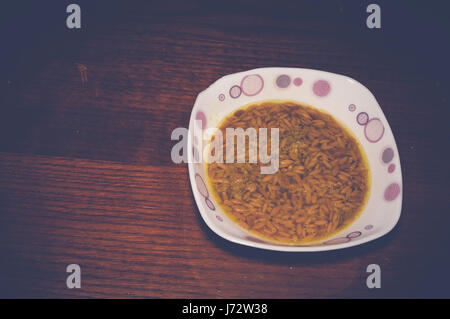 Soupe aux nouilles orzo dans bol blanc sur la table en bois Banque D'Images