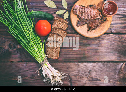 De veau poêlé sur une planche en bois, à côté des légumes frais et de tranches de pain, vue du dessus Banque D'Images