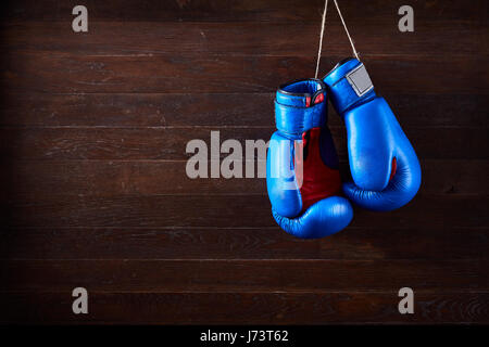 Une paire de gants de boxe rouge et bleu se bloque contre le fond de bois. Banque D'Images