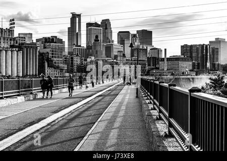 Les gens apprécient un sentier de randonnée pédestre et de vélo au Stone Arch Bridge de Minneapolis avec la ligne d'horizon à l'arrière-plan. Banque D'Images