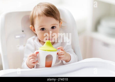 Bébé de boire la coupe de la tuyère dans une chaise haute à la maison Banque D'Images