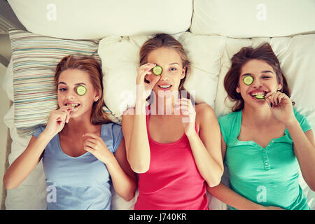 Heureux les jeunes femmes avec masque de concombre au lit Banque D'Images