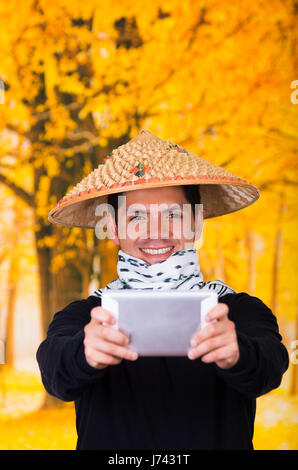 Portrait of a handsome hispanic young business guy portant un chapeau conique asiatiques pointant devant lui son Ipad à l'aide des deux mains en automne background Banque D'Images
