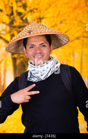 Portrait of a handsome hispanic young business guy portant un chapeau conique de l'Asie et de faire un signal de la victoire en automne background Banque D'Images