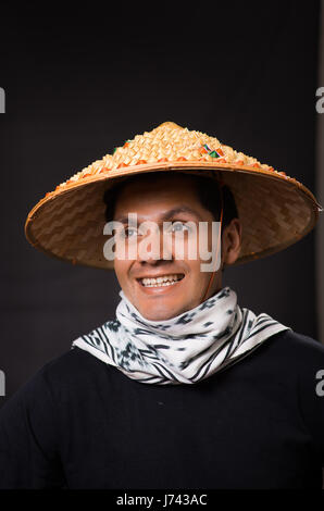 Portrait of a handsome smiling hispanic young business guy portant un chapeau conique d'Asie en fond noir Banque D'Images
