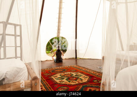 Femme méditant à l'entrée d'un grand tipi, glamping. Banque D'Images