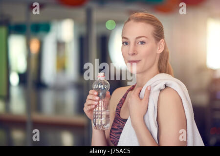 Jeune femme de boire de l'athlète de l'eau embouteillée pour bouteilles d'après l'entraînement dans une salle de sport dans un concept de santé et de remise en forme Banque D'Images