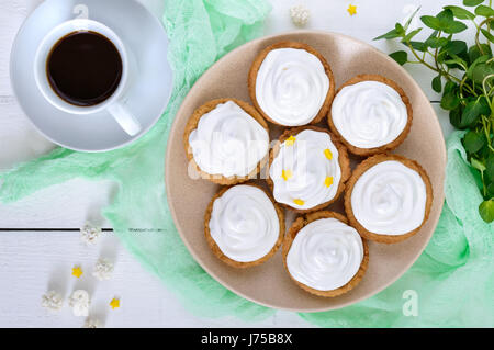 Mini tarte avec une crème d'air sur une assiette et une tasse de café sur un fond de bois blanc. La vue de dessus Banque D'Images