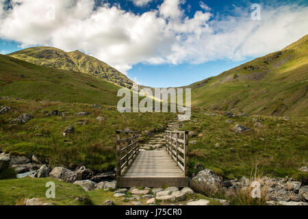 Paysage de Cumbrie dépeignant pont en bois rouge passage Tarn Beck et randonnées à vélo le long Catstye Glenridding Beck entre la came et le côté blanc (Keppel) Banque D'Images