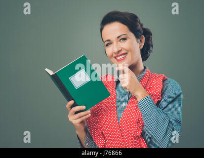 Rétro femme en souriant avec tablier et livre de hand on chin Banque D'Images