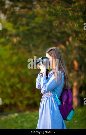 Belle jeune fille de prendre des photos dans la forêt. La jeune fille avec l'appareil photo. Touriste. Le coucher du soleil. Soirée d'été Banque D'Images