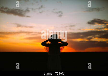 Silhouette girl wearing hat debout contre le ciel au coucher du soleil Banque D'Images