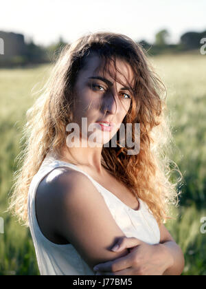 Jeune fille blonde à l'extérieur. Avec chapeau et robe blanche dans le champ de blé. Rétro-éclairée. Banque D'Images
