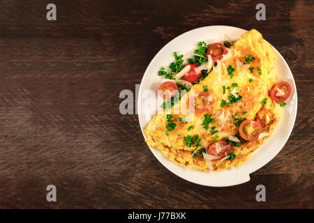 Une photo d'une omelette aux tomates cerises, le persil et le fromage râpé, tourné à partir de ci-dessus sur une texture rustique en bois avec une place pour le texte Banque D'Images