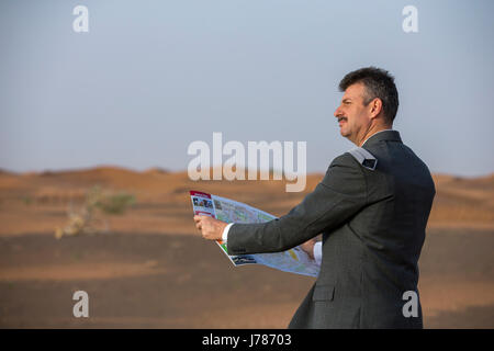 Businessman with a suitcase dans un désert, en regardant une carte d accès Banque D'Images