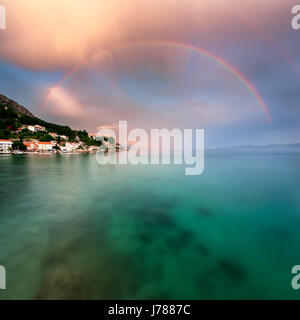 Arc-en-ciel sur plage rocheuse et d'un petit village après la pluie, la Dalmatie, Croatie Banque D'Images