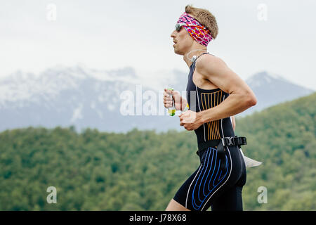 Jeune homme runner avec des éléments nutritifs de l'énergie dans l'exécution de la main en gel de printemps course marathon de montagne Banque D'Images