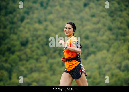 Girl runner avec de la musique dans les écouteurs sourit et s'exécutant dans Spring Mountain course marathon Banque D'Images