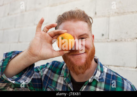 L'homme aux cheveux rouges avec une orange avant de l'œil Banque D'Images