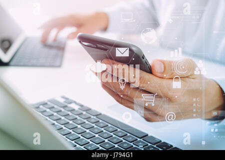 Close up of businessman using mobile phone and laptop computer on white bureau en bureau moderne avec schéma icônes VR Banque D'Images