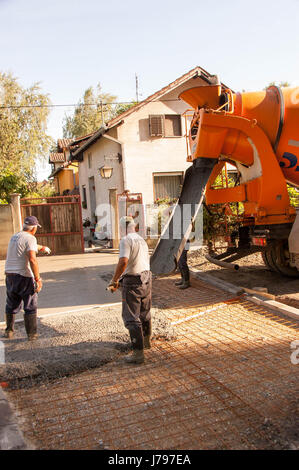 Travaux de bétonnage sur les places de parking en face de la chambre. Mise à niveau de l'ouvrier maçon béton avec truelles mason mains répandre du béton coulé. Banque D'Images