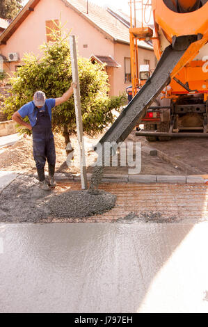 Travaux de bétonnage sur les places de parking en face de la chambre. Mise à niveau de l'ouvrier maçon béton avec truelles mason mains répandre du béton coulé. Banque D'Images