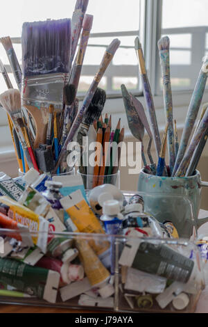Atelier d'artiste avec des pinceaux, de la peinture, crayons de couleur, crayons, couteaux et autres fournitures artistiques devant une fenêtre Banque D'Images