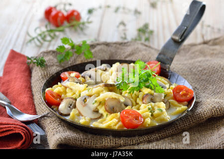 Spaetzle souabe végétarien avec épaississement sauce crème et champignons frais servi dans une poêle de fer sur une table rustique avec un vieux sac de jute Banque D'Images