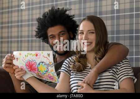 Smiling couple sitting on couch montrant pour l'encombrement Banque D'Images